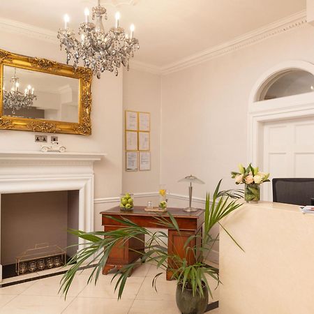 伦敦 巴比肯客房酒店 外观 照片 The photo shows a stylish reception area. There is a decorative chandelier hanging from the ceiling, providing elegant lighting. A large, ornate mirror is mounted on the wall beside the fireplace, which features a simple, classic design. In front of 