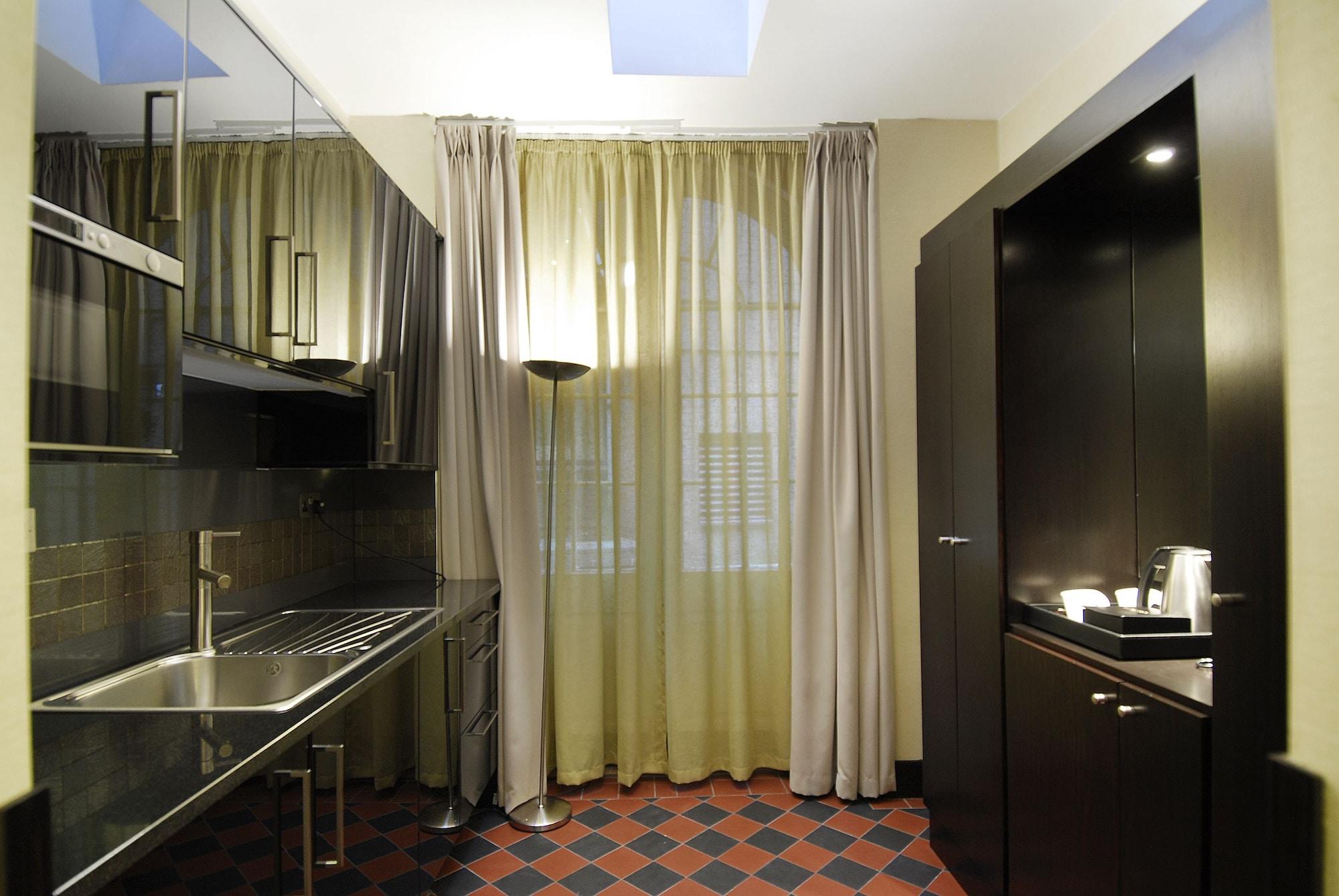 伦敦 巴比肯客房酒店 外观 照片 The photo shows a modern kitchen space. On the left side, there is a sleek countertop and kitchen cabinets in a dark finish. The backsplash appears shiny, reflecting the surroundings. To the right, there is a tall black cabinet. A window is covered w