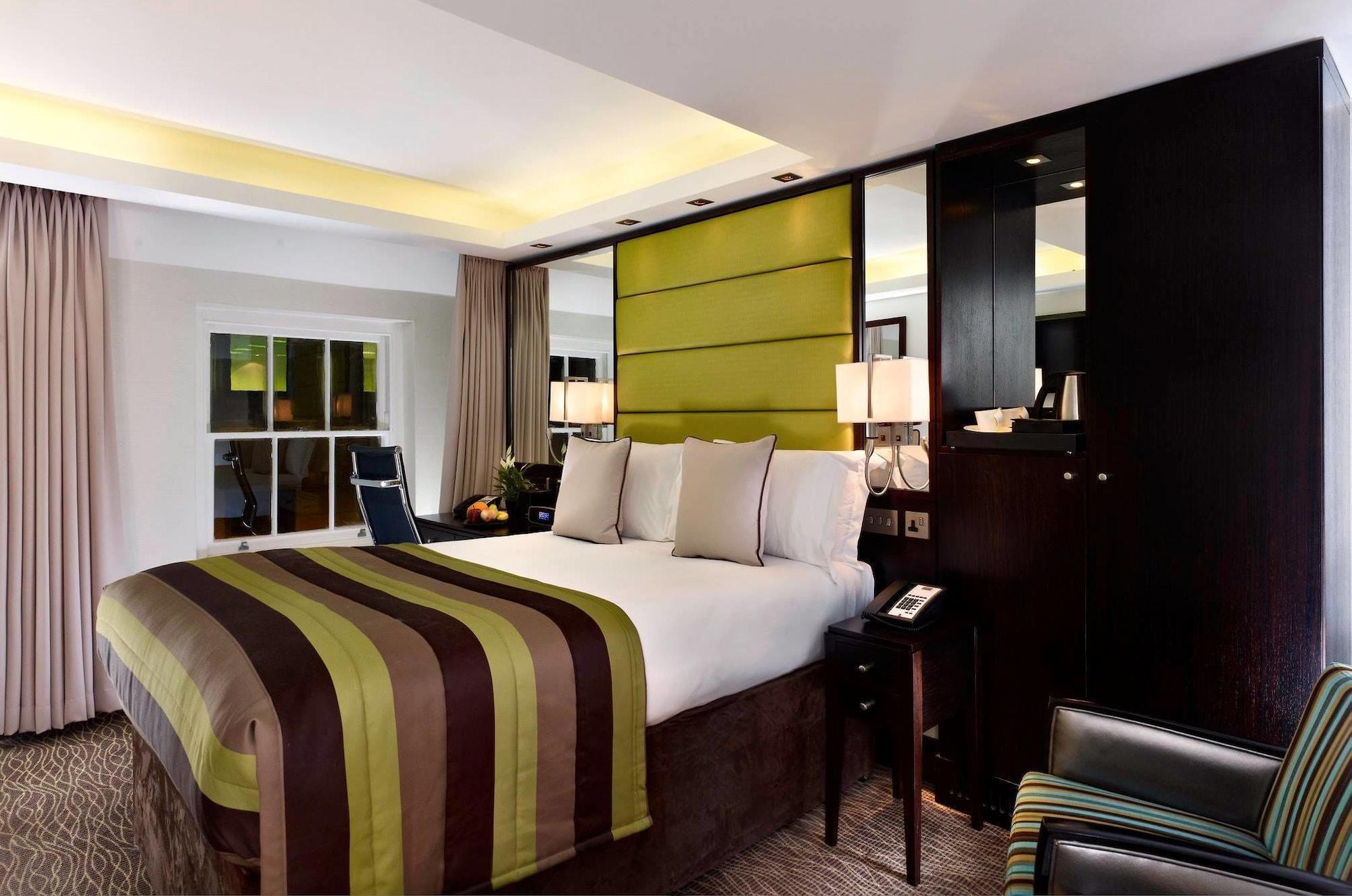 伦敦 巴比肯客房酒店 外观 照片 The photo shows a modern hotel room featuring a large bed with a striped comforter in shades of green, brown, and cream. The bed is adorned with several decorative pillows. Behind the bed, there is a contemporary headboard with a green panel design. 