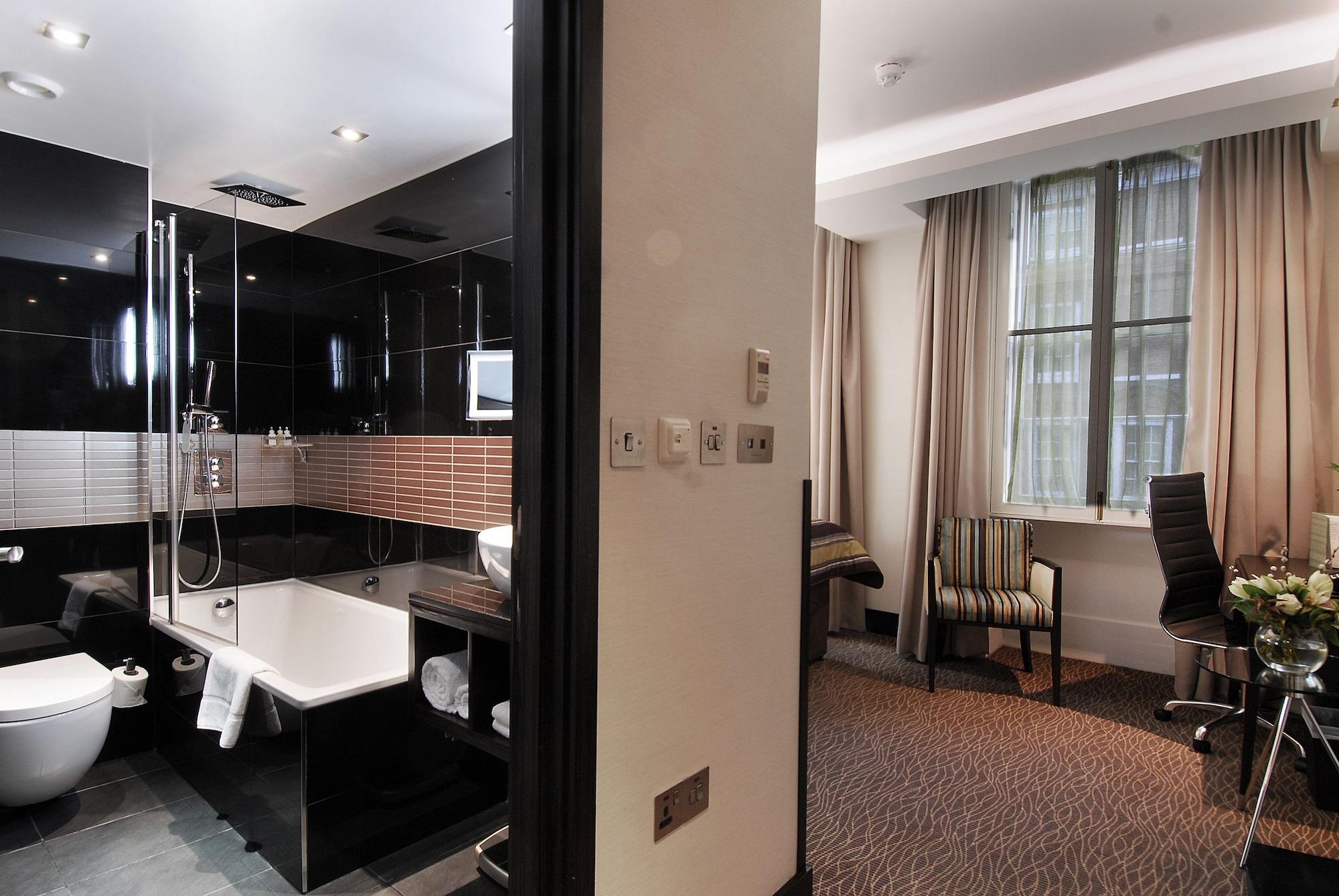 伦敦 巴比肯客房酒店 外观 照片 The photo shows a modern hotel room that features an elegant bathroom on one side and a living area on the other. 

1. **Bathroom**: The bathroom is stylishly designed with a combination of black and white tiles. It includes a bathtub, a shower area 