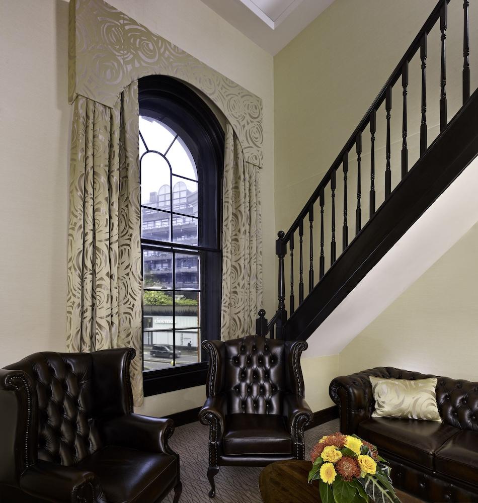 伦敦 巴比肯客房酒店 外观 照片 The photo shows a cozy interior space featuring two elegant leather armchairs placed near a large, ornate window with arched top and decorative curtains. The wall is painted in a muted color, enhancing the warmth of the room. A staircase with black s