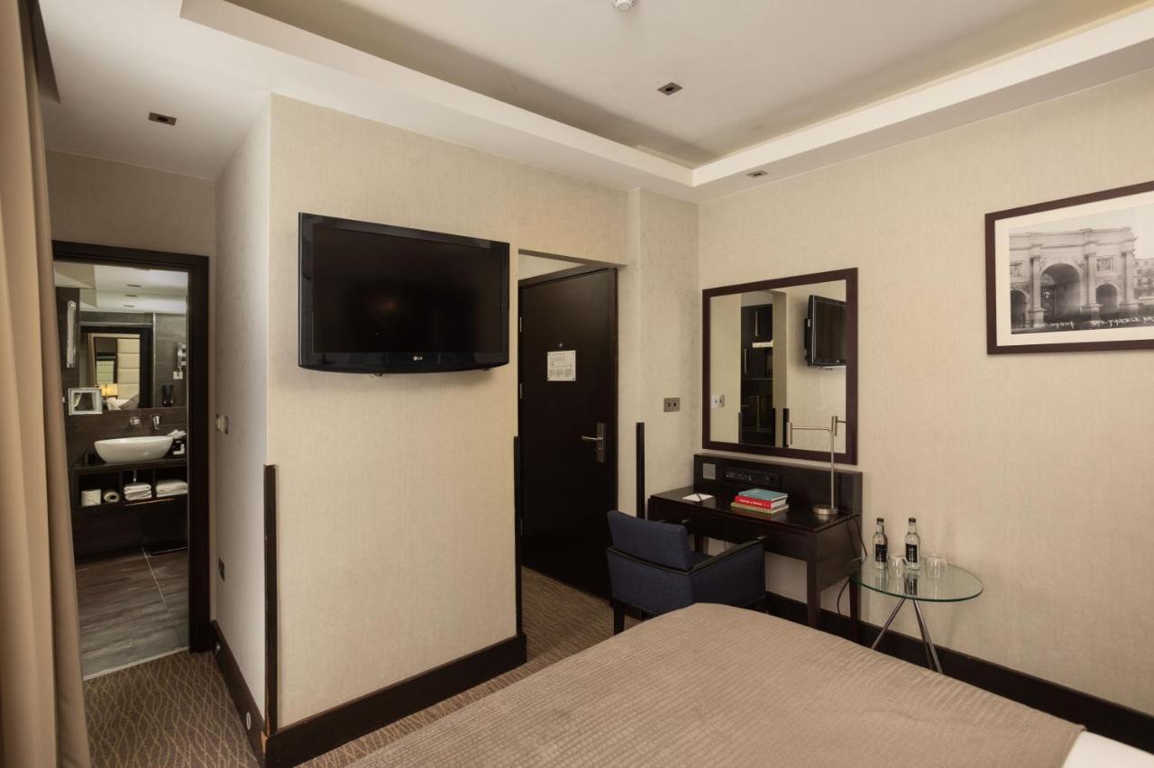 伦敦 巴比肯客房酒店 外观 照片 The photo shows a hotel room featuring a double bed with a neutral-colored bedspread. On one wall, there is a flat-screen TV mounted. Adjacent to the bed, there is a stylish desk with a chair and a small glass table. A mirror is positioned above the 