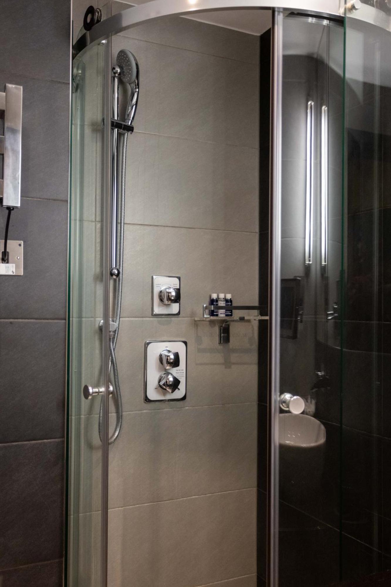 伦敦 巴比肯客房酒店 外观 照片 The photo shows a modern shower area. It features glass panels and tiled walls in a neutral color palette, creating a sleek and contemporary look. There are two main control panels for adjusting the water temperature and pressure, with various knobs 