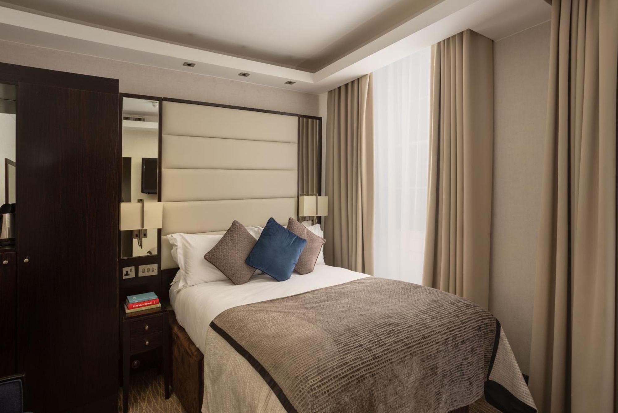 伦敦 巴比肯客房酒店 外观 照片 The photo shows a modern hotel room with a cozy design. It features a double bed with a light-colored headboard and a soft, stylish blanket. There are decorative pillows on the bed, including a blue one. On either side of the bed, there are small nig
