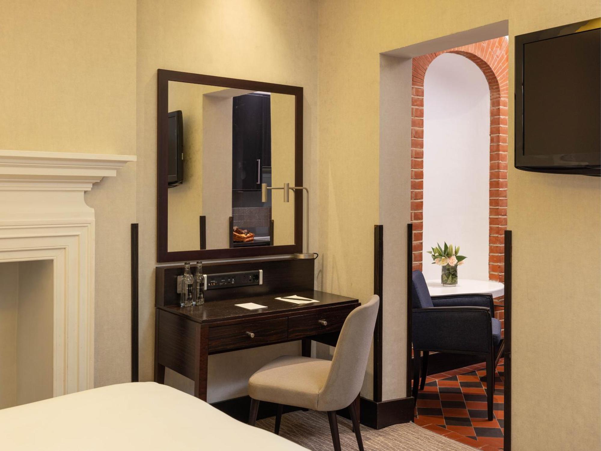 伦敦 巴比肯客房酒店 外观 照片 The photo displays a hotel room setup. On the left side, there's a bed with a simple white bedding arrangement. Adjacent to the bed, there's a wooden desk with a chair, along with a mirror above the desk. The desk area is equipped with some glassware