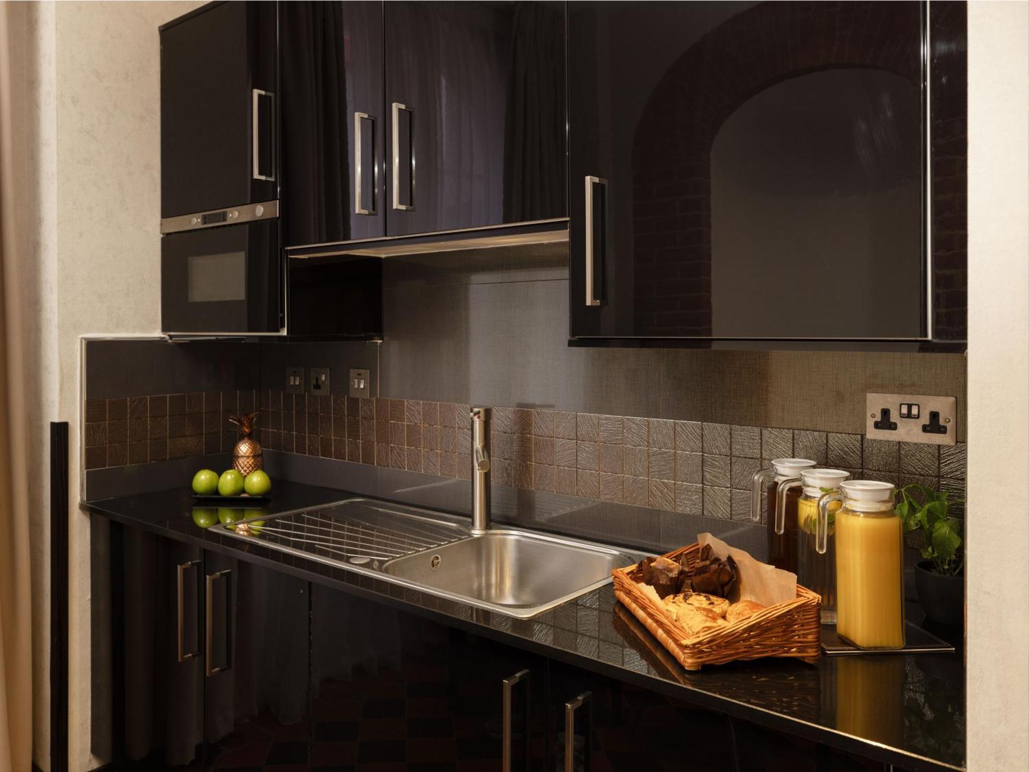 伦敦 巴比肯客房酒店 外观 照片 The photo shows a modern kitchen with sleek black cabinetry and a glossy finish. The kitchen features a stainless steel sink with a contemporary faucet, set against a dark, textured countertop. Above the counter, there are cabinets that match the cou