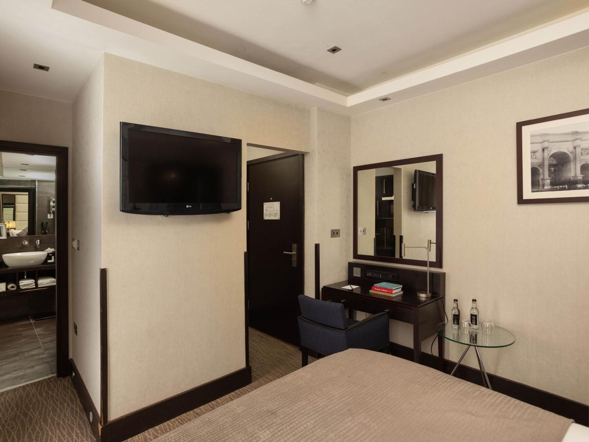 伦敦 巴比肯客房酒店 外观 照片 The photo shows a hotel room with a modern and minimalist design. On the left, there's a wall-mounted flat-screen TV. In the center, there's a bed with a neutral-colored bedspread. To the right of the bed, there is a small desk with a mirror above it