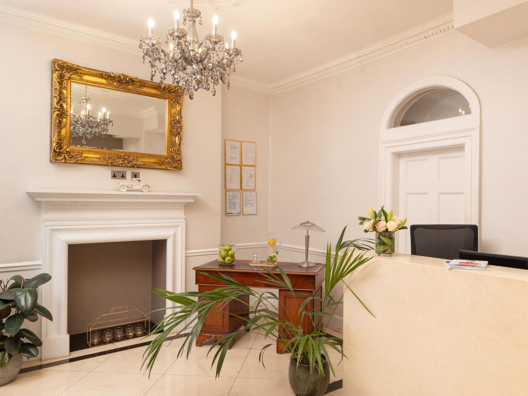 伦敦 巴比肯客房酒店 外观 照片 The photo shows a stylish reception area. There is a decorative chandelier hanging from the ceiling, providing elegant lighting. A large, ornate mirror is mounted on the wall beside the fireplace, which features a simple, classic design. In front of 