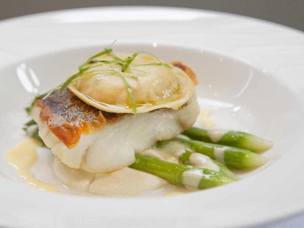 伦敦 巴比肯客房酒店 外观 照片 The image shows a beautifully presented dish featuring a piece of fish, likely a white fish, topped with a clam. It is served on a bed of green asparagus spears. The dish is garnished with thinly sliced herbs or greens, adding a touch of color. The s
