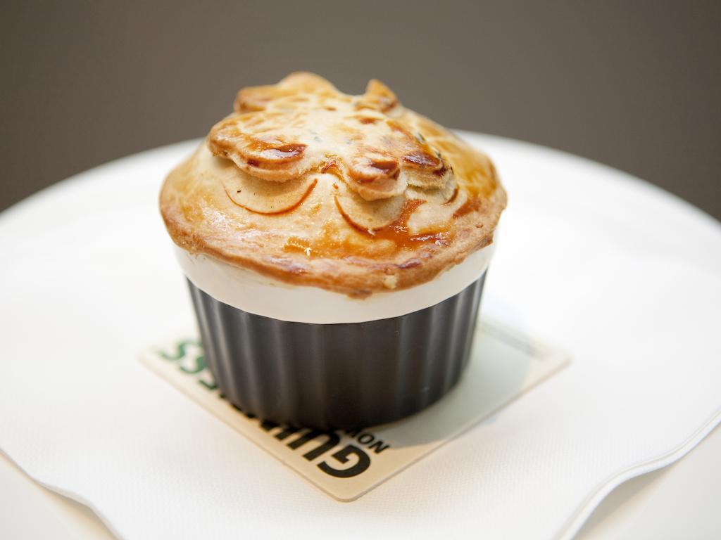 伦敦 巴比肯客房酒店 外观 照片 The photo shows a small, individual serving of a pie, likely a savory dish. It has a golden-brown crust with decorative elements on top, resembling leaves or floral patterns. The pie is served in a black dish and placed on a white plate. The overall 