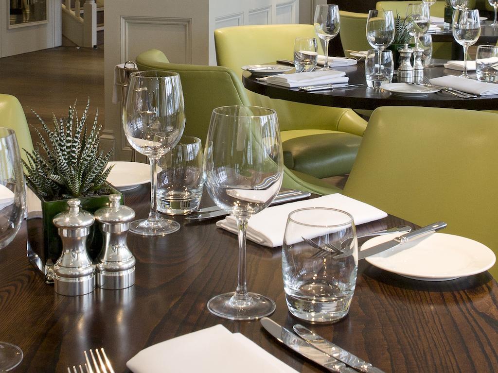 伦敦 巴比肯客房酒店 外观 照片 The photo shows a dining setup in a restaurant. There are tables with a polished wooden surface and elegant place settings. Each setting includes multiple wine glasses and water glasses, neatly arranged with folded napkins. 

In the center, there are