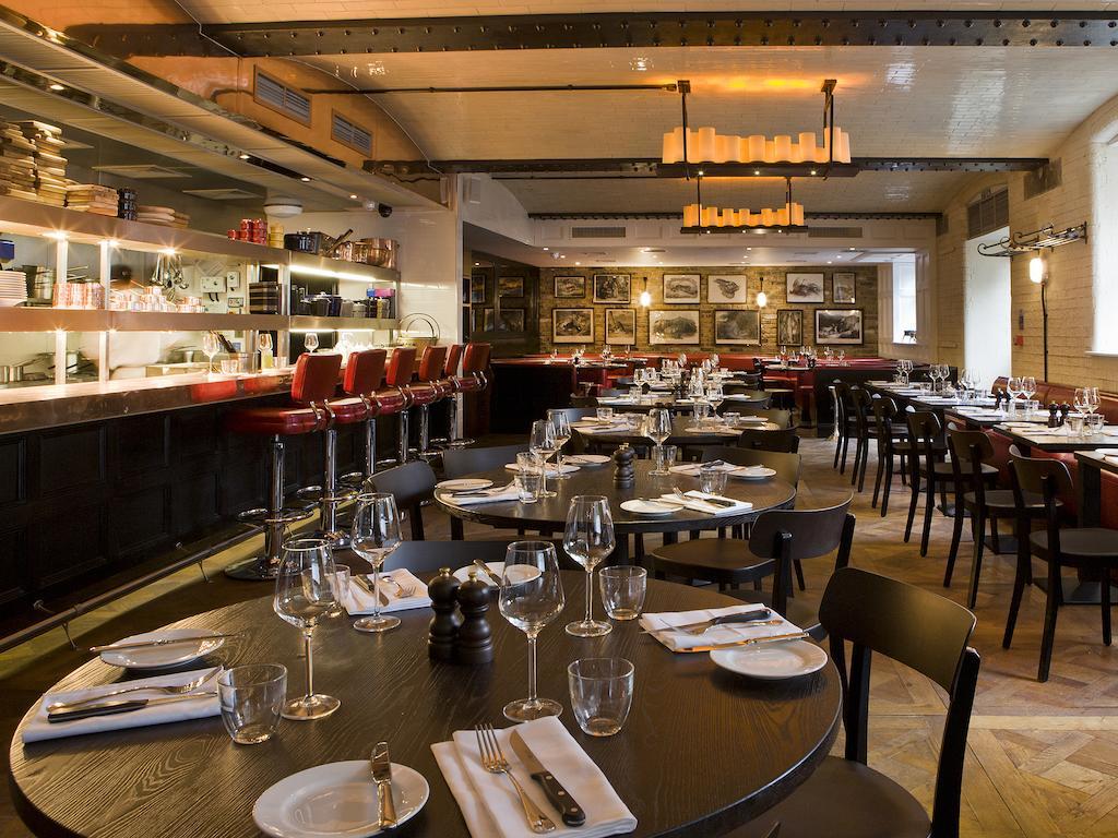 伦敦 巴比肯客房酒店 外观 照片 The photo shows the interior of a stylish restaurant. It features several round tables set with white plates, glasses, and silverware, all neatly arranged for dining. The decor includes a modern design with wooden floors and a mix of lighting fixture