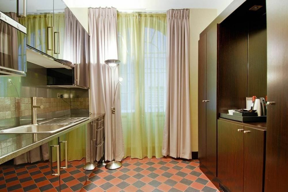 伦敦 巴比肯客房酒店 外观 照片 The photo shows a modern kitchen area. There is metallic cabinetry and a stainless steel countertop with a sink. The walls are adorned with light-colored curtains that allow natural light to filter in, with one set in a soft purple hue and another in