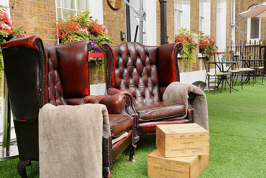 伦敦 巴比肯客房酒店 外观 照片 The photo depicts two large, elegant armchairs with a classic design, featuring rich burgundy leather upholstery and button tufting. They are positioned in a cozy outdoor setting, with lush green artificial grass beneath them. Next to the chairs, the